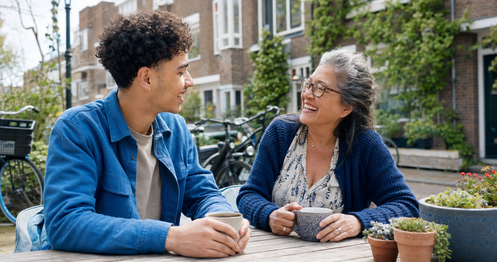 Een jongere en een oudere drinken koffie en praten samen in een Tilburgse wijk.